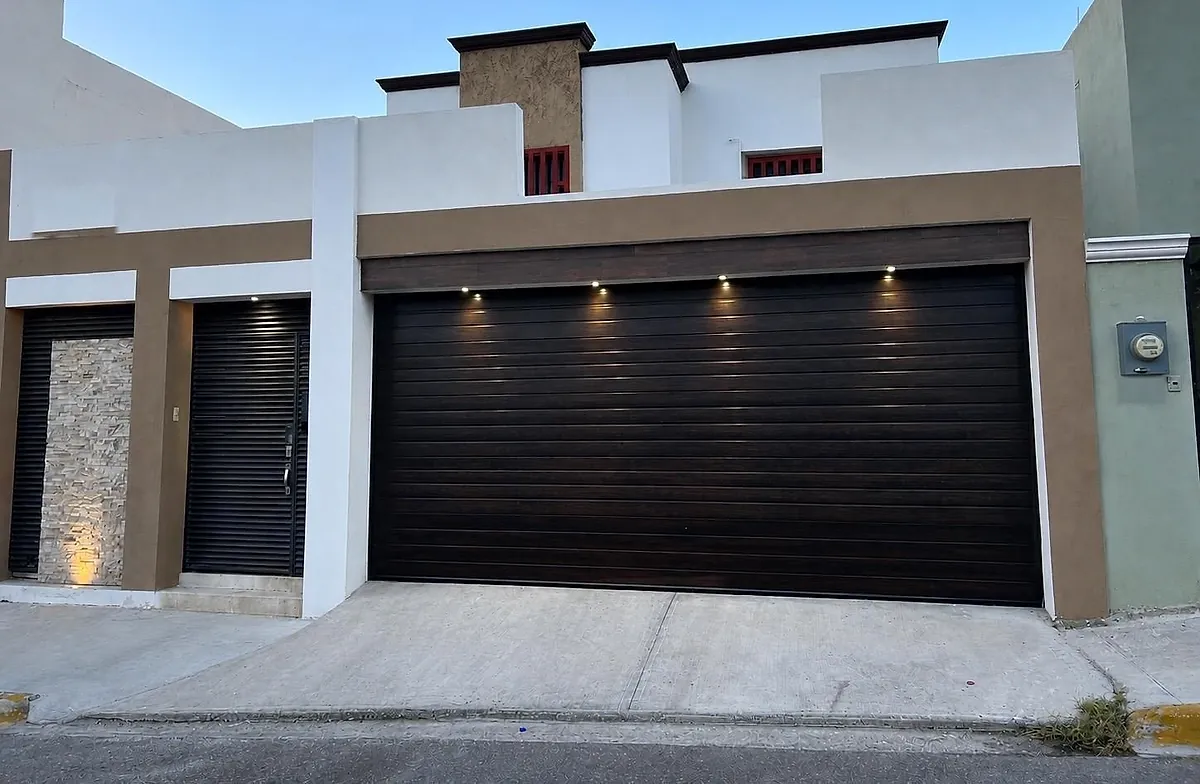 Casa al anochecer con portón americano café oscuro e iluminación integrada